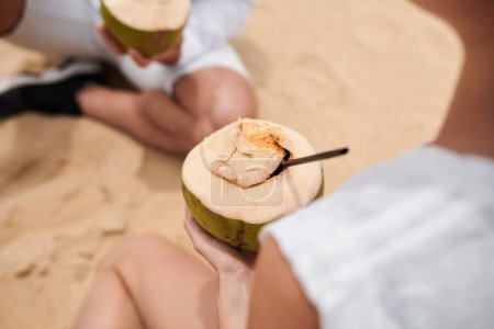 Téléchargez les photos : Boisson à la noix de coco entre les mains d'une jeune femme reposant sur la plage - en image libre de droit