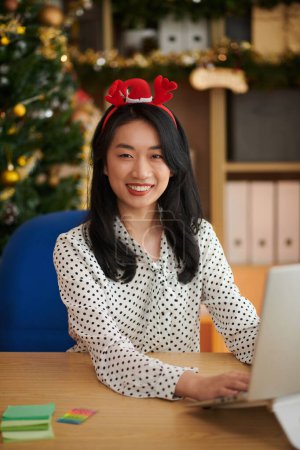 Photo for Portrait of joyful female entrepreneur working on laptop in office on Christmas day - Royalty Free Image