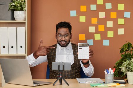 Téléchargez les photos : Homme d'affaires montrant calculatrice avec somme des dépenses à l'écran lors de la prise de collègues en ligne - en image libre de droit