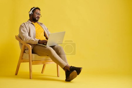 Foto de Desarrollador de software escuchando música en auriculares y trabajando en laptop, aislado en amarillo - Imagen libre de derechos