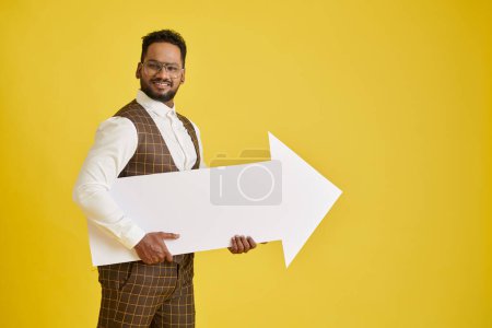 Foto de Empresario excitado sosteniendo enorme flecha de papel blanco, aislado en amarillo - Imagen libre de derechos