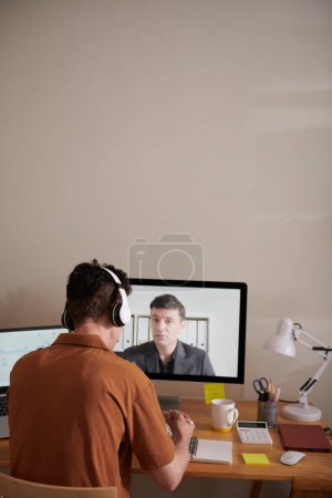 Foto de Joven tomando notas en el planificador cuando habla con su colega durante la reunión en línea - Imagen libre de derechos