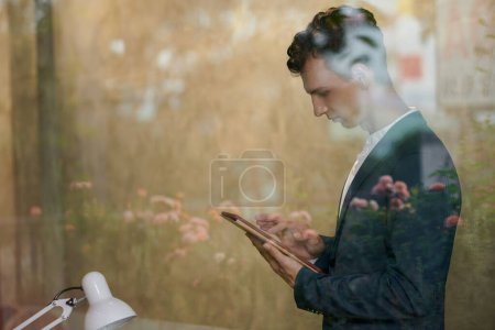 Téléchargez les photos : Sérieux jeune homme d'affaires lecture article sur tablette - en image libre de droit