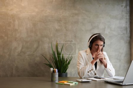 Téléchargez les photos : Femme d'affaires pensive dans les écouteurs lisant le document ou le rapport sur l'écran d'ordinateur portable - en image libre de droit