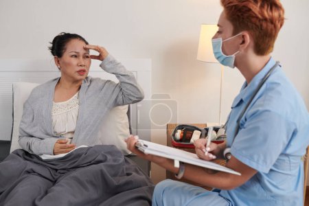 Téléchargez les photos : Femme âgée se plaignant de maux de tête au médecin lui rendant visite à la maison - en image libre de droit
