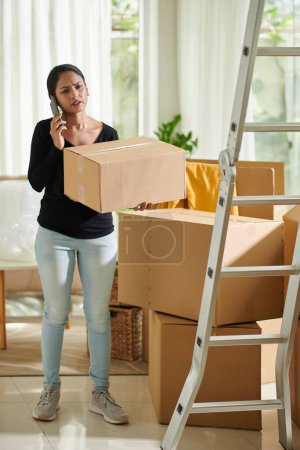 Photo for Frowning woman packing belongings and calling to moving company - Royalty Free Image