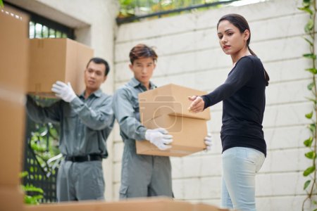 Téléchargez les photos : Propriétaire de la maison montrant déménageurs quand mettre des boîtes en carton - en image libre de droit