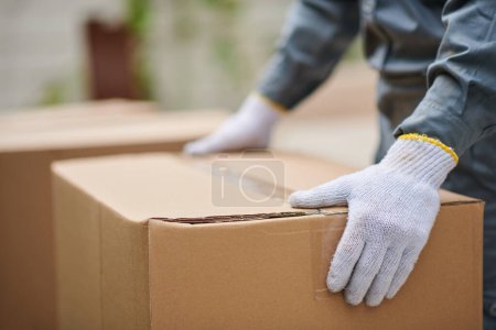 Téléchargez les photos : Déménageur portant des gants textiles lors de l'emballage et du transport de boîtes en carton - en image libre de droit