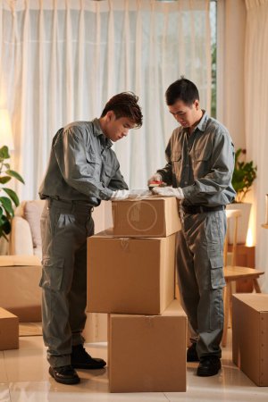 Photo for Team of movers packing and sealing cardboard boxes - Royalty Free Image