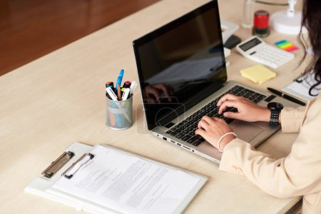 Téléchargez les photos : Gros plan de la jeune femme d'affaires travaillant en ligne à l'aide d'un ordinateur portable alors qu'elle était assise sur son lieu de travail au bureau - en image libre de droit