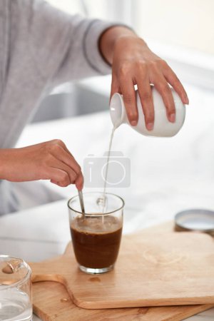 Foto de Primer plano de la mujer joven añadiendo leche en taza con cacao en la mesa, ella haciendo bebida para el desayuno - Imagen libre de derechos
