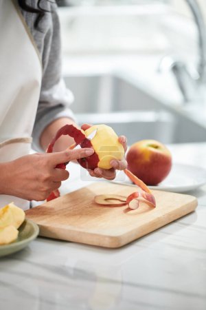 Foto de Primer plano de la mujer joven cortando la cáscara de manzana en la tabla de cortar en la mesa - Imagen libre de derechos