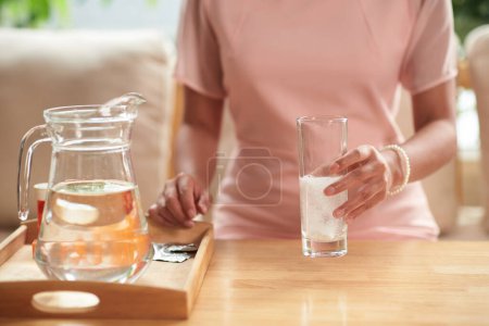 Foto de Primer plano de la joven sosteniendo un vaso de agua y tomando medicamentos por la mañana en casa - Imagen libre de derechos