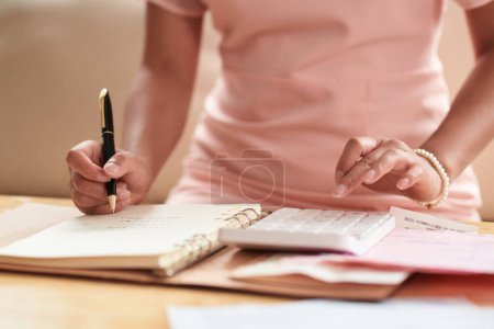 Photo for Close-up of young woman making notes in notepad, she planning her finance at table - Royalty Free Image