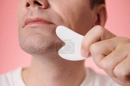Photo for Closeup image of mature man massaging jaw line with gua sha tool - Royalty Free Image