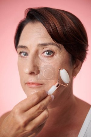 Photo for Face of mature woman doing massage with rose quartz roller - Royalty Free Image