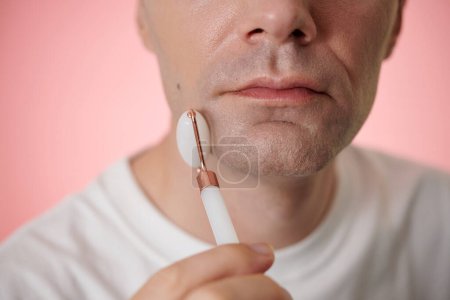 Photo for Face of middle-aged man massaging low third of his face with quartz roller - Royalty Free Image