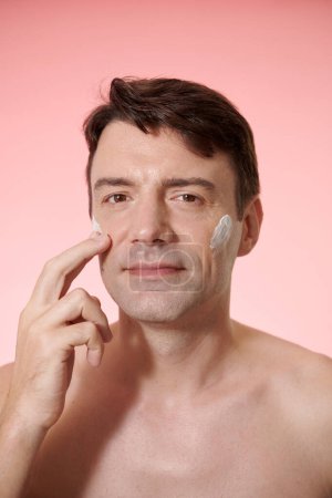 Téléchargez les photos : Portrait d'homme mature appliquant un masque éclaircissant après la douche de nuit - en image libre de droit