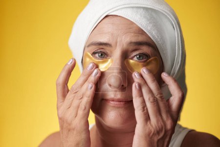 Photo for Portrait of mature woman with towel on head applying hydrogel patches after shower - Royalty Free Image