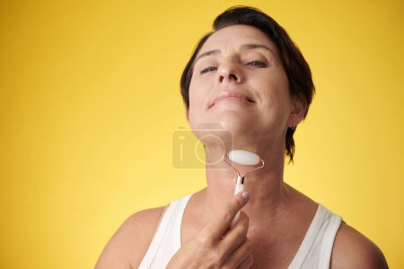 Photo for Happy mature woman massaging her neck with roller to reduce wrinkles - Royalty Free Image