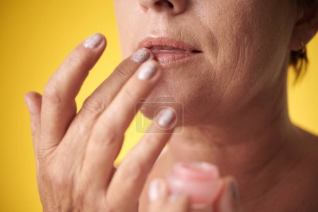 Téléchargez les photos : Image recadrée d'une femme mature appliquant un baume à lèvres pour hydrater la peau - en image libre de droit
