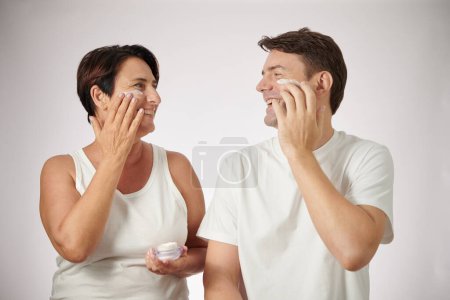 Foto de Mujer madura alegre mirándose el uno al otro al aplicar crema hidratante facial - Imagen libre de derechos