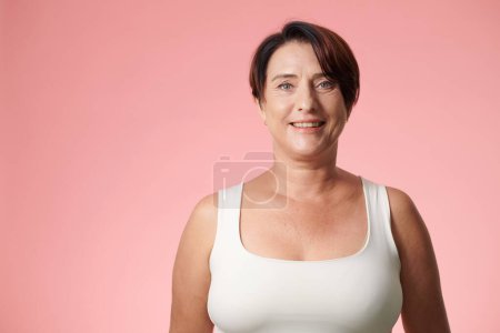 Foto de Retrato de mujer madura sonriente en top blanco sobre fondo rosa - Imagen libre de derechos