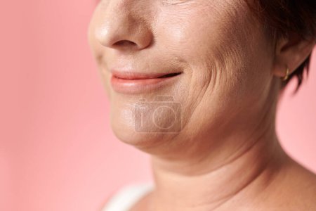 Téléchargez les photos : Image recadrée d'une femme mûre souriante debout sur fond rose - en image libre de droit