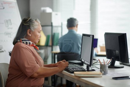 Téléchargez les photos : Femme âgée concentrée travaillant sur ordinateur en classe pour débutants - en image libre de droit
