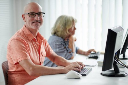 Téléchargez les photos : Portrait d'un homme âgé souriant travaillant sur ordinateur en classe pour débutant - en image libre de droit