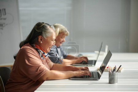 Foto de Feliz mujer mayor aprendiendo a trabajar en el ordenador portátil en clase para principiantes - Imagen libre de derechos