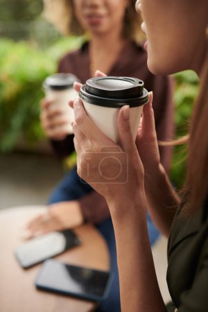 Foto de Primer plano de dos amigos tomando café de tazas desechables durante su reunión en la cafetería - Imagen libre de derechos