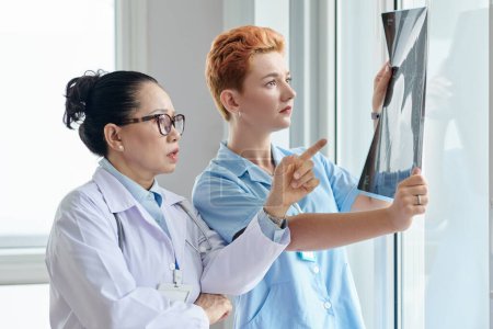 Foto de Profesional médico asiático discutiendo imagen de rayos X junto con la enfermera en la oficina - Imagen libre de derechos