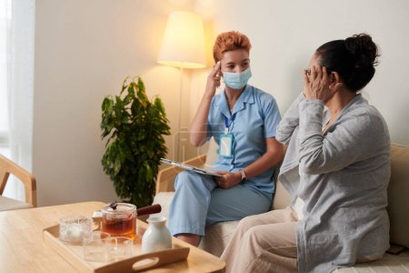 Téléchargez les photos : Une patiente âgée parle de maux de tête à une infirmière lors de sa visite à domicile - en image libre de droit
