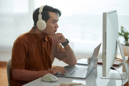 Téléchargez les photos : Pensif jeune homme dans les écouteurs revoir le code de programmation de son collègue - en image libre de droit