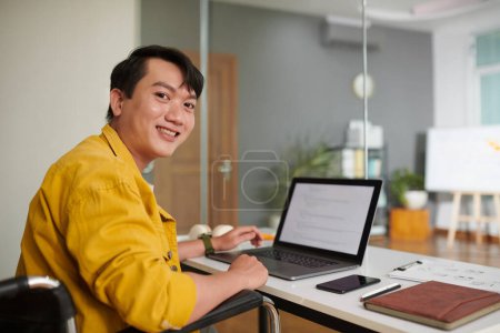 Photo for Cheerful young man with disability working on computer in office - Royalty Free Image