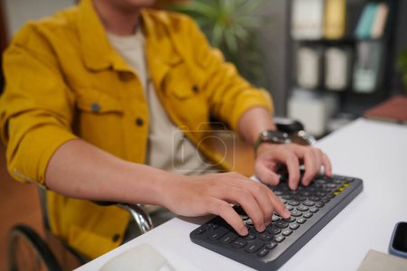 Téléchargez les photos : Image rapprochée d'un homme handicapé travaillant sur ordinateur au bureau, répondant à des courriels et codant - en image libre de droit