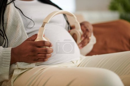 Téléchargez les photos : Image recadrée de la femme enceinte plaçant des écouteurs sur le ventre et allumant la musique classique - en image libre de droit