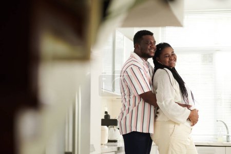 Téléchargez les photos : Joyeux couple noir anticipant enfant debout dans la cuisine - en image libre de droit