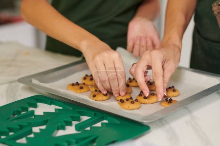 Téléchargez les photos : Mains de mère et fille décorant les biscuits avec des pépites de chocolat - en image libre de droit