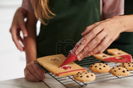 Photo for Closeup image of mother teaching daughter decorating gingerbread house with icing - Royalty Free Image