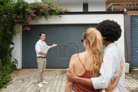 Foto de Sonriente agente de bienes raíces mostrando casa a pareja joven - Imagen libre de derechos
