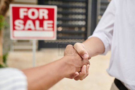Téléchargez les photos : Image rapprochée d'un agent immobilier saluant un client devant une maison à vendre - en image libre de droit