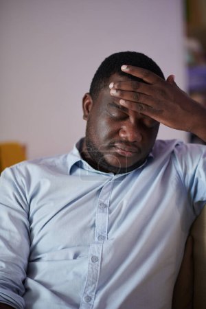 Téléchargez les photos : Homme noir stressé et fatigué souffrant de maux de tête après une dure journée de travail - en image libre de droit