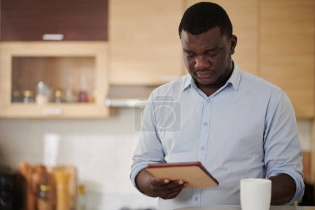 Foto de Hombre de negocios serio leyendo artículo de noticias en la tableta al beber taza de café de la mañana - Imagen libre de derechos
