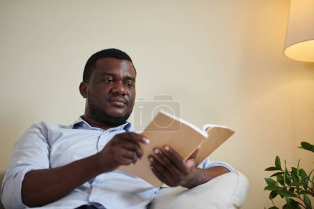 Photo for Portrait of serious Black businessman reading popular novel at home - Royalty Free Image