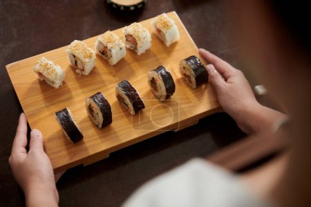 Téléchargez les photos : Serveuse mettant le conseil de sushi de bambou sur la table de café - en image libre de droit