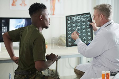 Photo for Doctor talking to military man about back pain and showing spine discs MRI image that helps to track recovery - Royalty Free Image