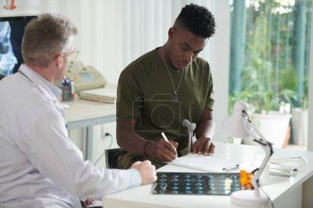 Photo for Black military man signing documents in medical office - Royalty Free Image
