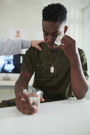Photo for Crying military man wiping off tears and drinking glass of water in medical office - Royalty Free Image